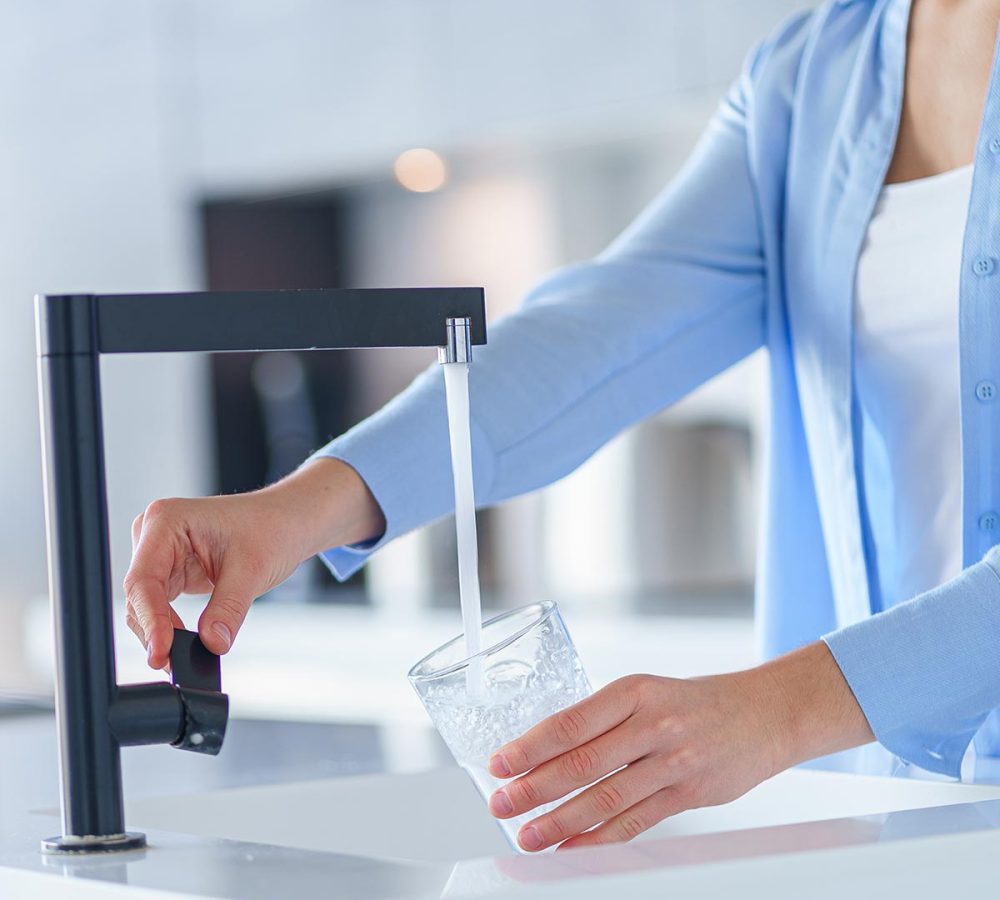 Female pours fresh filtered purified water from a tap into a glass at kitchen at home